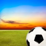 Soccer Ball With Green Grass Field Against Sunset Sky Stock Photo