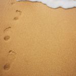 Sea Wave With Foam And Human Footprints On Sand Stock Photo