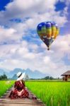 Young Woman Look At Balloon And Sitting On Wooden Path With Green Rice Field In Vang Vieng, Laos Stock Photo