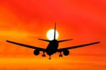 Silhouetted Commercial Airplane Flying At Sunset Stock Photo