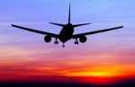 Silhouetted Commercial Airplane Flying At Sunset Stock Photo