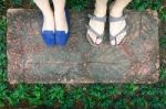 Top View Feet Of Male And Female Couple Lover Standing On Stone Floor Among Little Green Grass Garden. Hipster Style Stock Photo