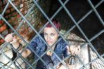 Punk Girl Sitting On The Floor Behind Metal Bars Stock Photo