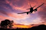 Silhouetted Commercial Airplane Flying At Sunset Stock Photo