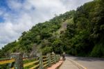 Monkey Sitting On The Side Of A Highway With Tall Hill In The Ba Stock Photo