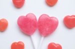 Pink Valentine's Day Heart Shape Lollipop With Small Red Candy In Cute Pattern On Empty White Paper Background. Love Concept. Colorful Hipster Style. Knolling Top View Stock Photo