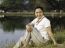 Woman Sitting On Green Field By Lake