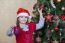 Little Girl In Santa Hat Near Christmas Tree