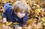 Toddler Blond Boy With Blue Eyes Lays On Bed Of Autumn Fallen Le