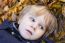 Small Blond Boy With Blue Eyes Lays On Bed Of Autumn Fallen Leav