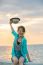 Portrait Of Beautiful And Happy Emotion Teenager Wearing Straw Hat Sitting On Bridge Beside Sea Beach Against Sun Set Sky