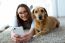 Beautiful Young Woman With Her Dog Using Mobile Phone At Home