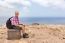 Man With Backpack Sitting Uphill At Sea Coast