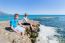 Mother And Son As Tourists Sitting On Rock At Blue Sea