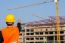 Young Engineer In Orange Shirt Stands Pointing At A Building Bei