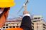 Young Engineer In Orange Shirt Stands Pointing At A Building Bei