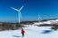 Beautiful Girl Walking In Winter Landscape Of Sky And Winter Road With Snow And Red Dress And Wind Turbine