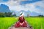 Young Woman Sitting On Wooden Path With Green Rice Field In Vang Vieng, Laos