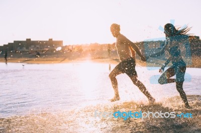 A Couple Is Running On Beach While The Sun Is Set Stock Photo