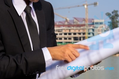 A Young Businessman Holds And Points To A Blueprint Of A Buildin… Stock Photo