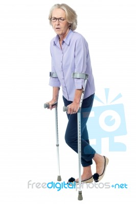 Aged Woman In Pain Walking With Crutches Stock Photo