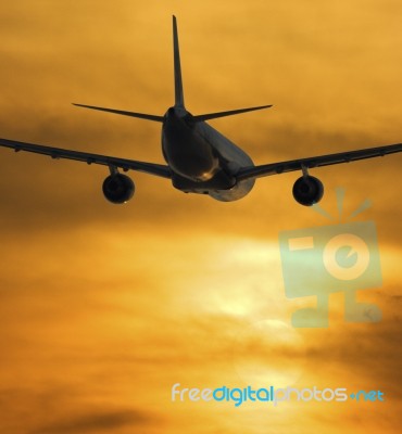 Airplane Flying Towards Sunset Stock Photo