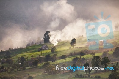 Alpine Village In Mountains. Smoke, Bonfire And Haze Over Hills Stock Photo