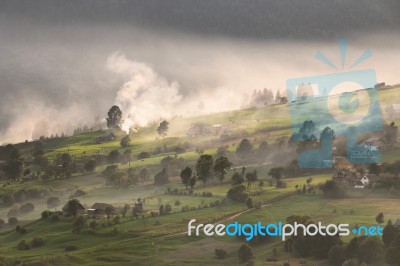 Alpine Village In Mountains. Smoke, Bonfire And Haze Over Hills Stock Photo