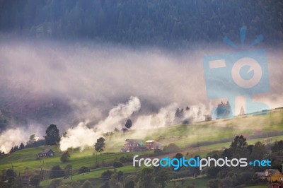 Alpine Village In Mountains. Smoke, Bonfire And Haze Over Hills Stock Photo