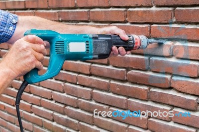 Arms Holding Drilling Machine Against Brick Wall Stock Photo