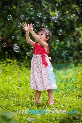 Asian Girl Catches Soap Bubbles On Nature Background. Outdoors Stock Photo