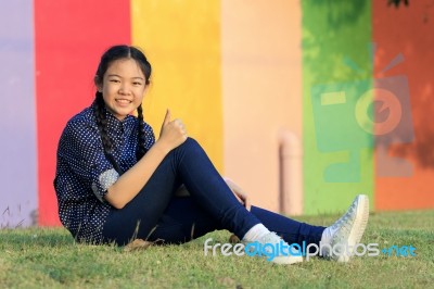 Asian Girl Relaxing Sitting On Green Grass Field Of Public Park And Hand Sign Ok ,all Right With Toothy Smiling Face Happiness Emotion Stock Photo