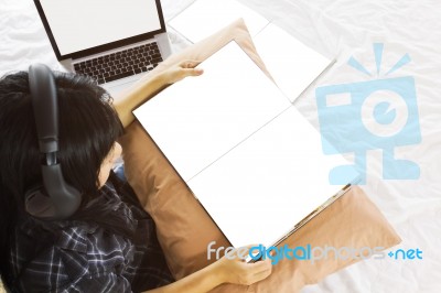 Asian Girl Sitting On Bed Reading Blank Book Listening To Music Stock Photo