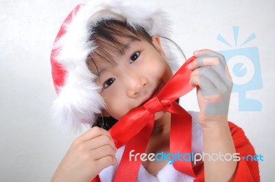 Asian Little Girl Dressed In Santa Claus Holding Red Ribbon Stock Photo