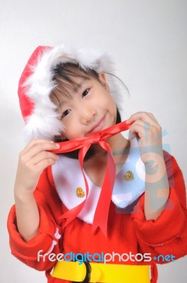 Asian Little Girl Dressed In Santa Claus Holding Red Ribbon Stock Photo