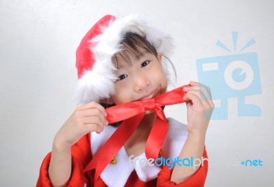 Asian Little Girl Dressed In Santa Claus Holding Red Ribbon Stock Photo