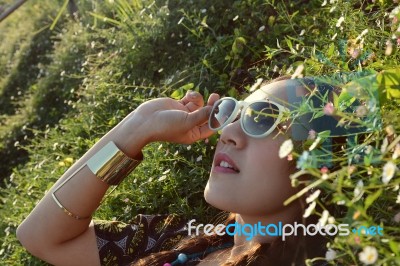 Asian Woman Wear Sunglasses Lying In The Flower Garden Stock Photo