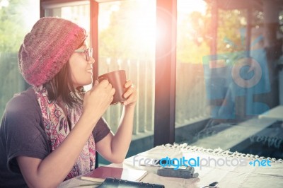 Asian Younger Woman And Hot Coffee Mug In Hand Smiling With Happiness Emotion Sitting Beside Mirror Window Against Beautiful Sun Light ,process Warming Color Mood And Tone Stock Photo