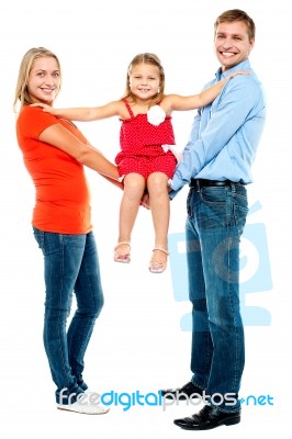 Baby Girl Sitting On Outstretched Arms Of Her Parents Stock Photo