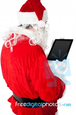 Back View Of Santa Looking At Tablet Device Screen Stock Photo