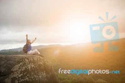 Backpacker Woman Relaxing And Victory Hand Rising On Rock Cliff And Sun Set Sky Above Stock Photo