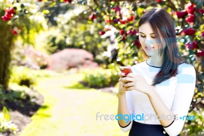 Beautiful Girl Typing Text Message On Her Smart Phone In The Gar… Stock Photo