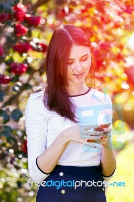 Beautiful Girl Typing Text Message On Her Smart Phone In The Gar… Stock Photo