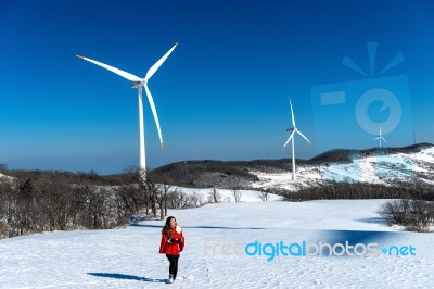 Beautiful Girl Walking In Winter Landscape Of Sky And Winter Road With Snow And Red Dress And Wind Turbine Stock Photo