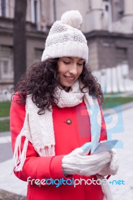 Beautiful Woman In Red Coat And Wool Cap And Gloves With Smartph… Stock Photo