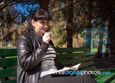 Beautiful Woman Sitting On A Park Bench Holding A Pen And Notebo… Stock Photo