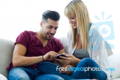 Beautiful Young Couple Using Mobile Phone At Home Stock Photo