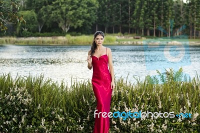 Beautiful Young Woman In The Gardens Wearing A Long Silk Red Dress Stock Photo