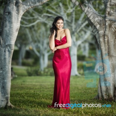 Beautiful Young Woman In The Gardens Wearing A Long Silk Red Dress Stock Photo