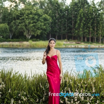 Beautiful Young Woman In The Gardens Wearing A Long Silk Red Dress Stock Photo